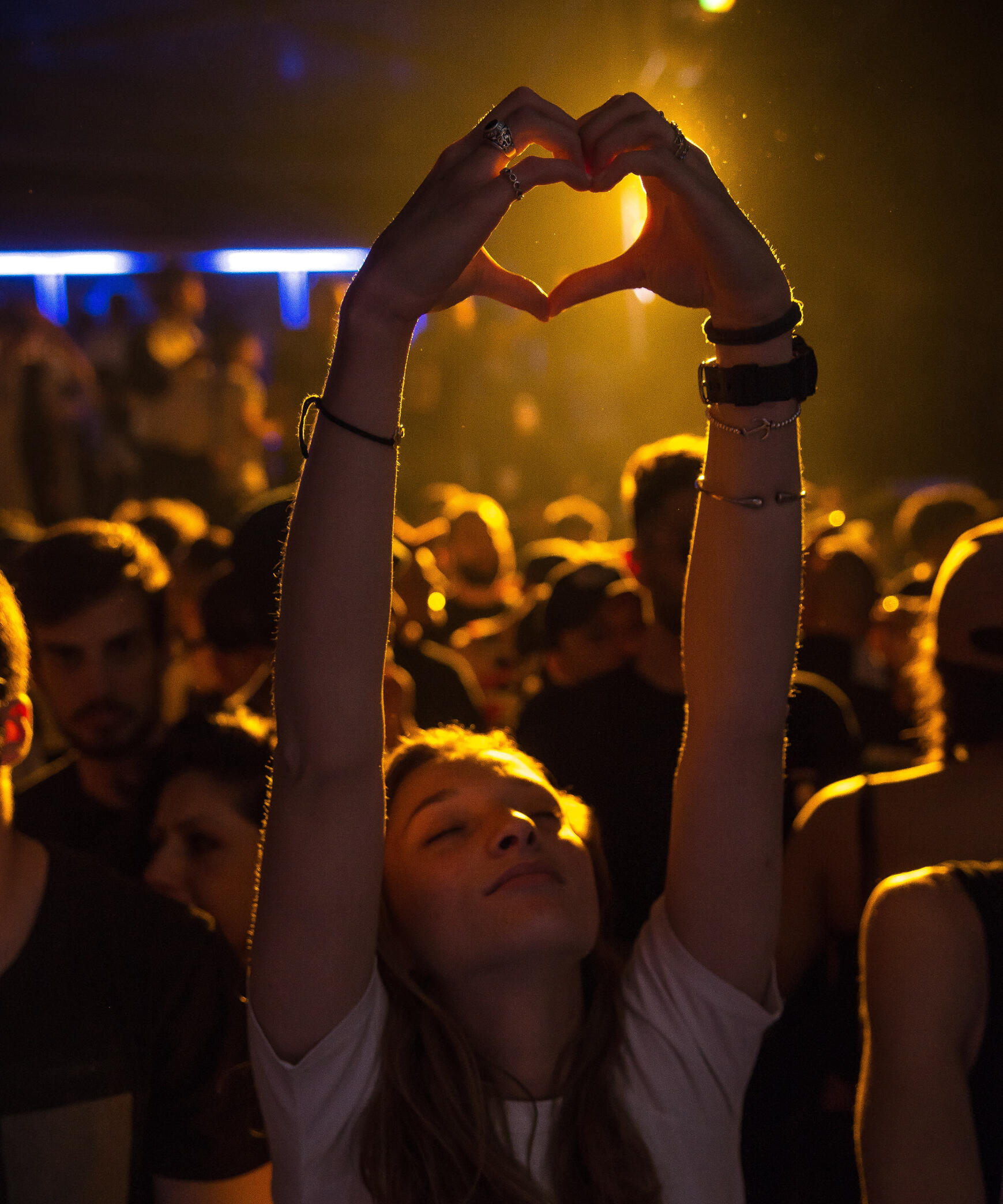 A crowd listening to music with a girl hoiding up a heart shape with her hands.
