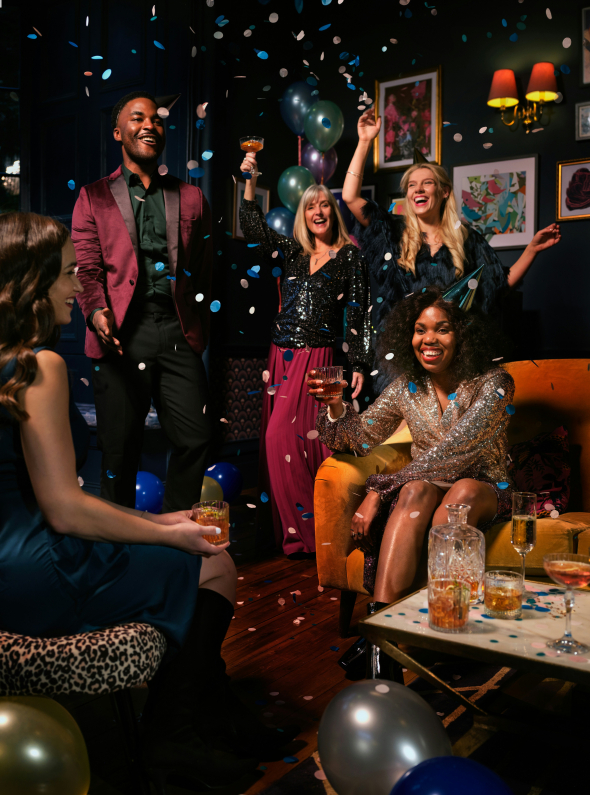 People toasting with champagne and cocktails and having fun at a party with balloons and confetti