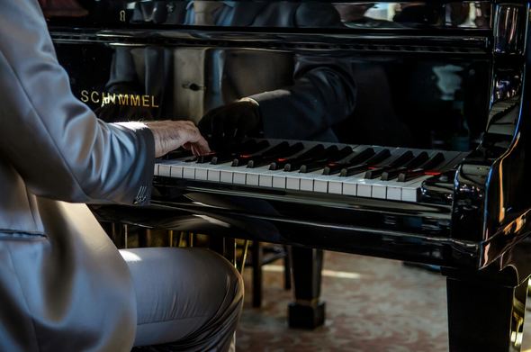 Man in a grey suit playing a Schimmel grand piano.